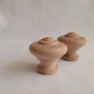 May include: Two wooden knobs with a rounded, spiral design. The knobs are light brown and have a smooth finish.