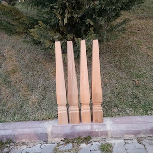 Puede incluir: Cuatro patas de mesa de madera sin terminar con un diseño cónico y tallas decorativas en la parte inferior.