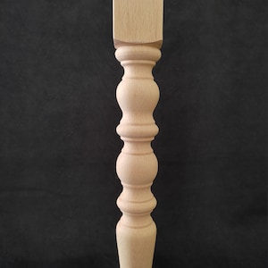 K&ouml;nnte beinhalten: Ein Tischbein aus Holz mit quadratischer Oberseite und gedrehtem, geriffeltem Design. Das Bein ist unbehandelt und hat eine nat&uuml;rliche Holzfarbe.