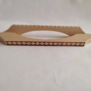 Könnte beinhalten: Ein Holzständer mit einer Diamant-Muster-Einlage. Der Ständer hat eine abgerundete Öffnung in der Mitte.