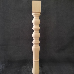 K&ouml;nnte beinhalten: Ein Tischbein aus Holz mit gedrehtem Design. Das Bein ist unbehandelt und hat eine quadratische Oberseite.