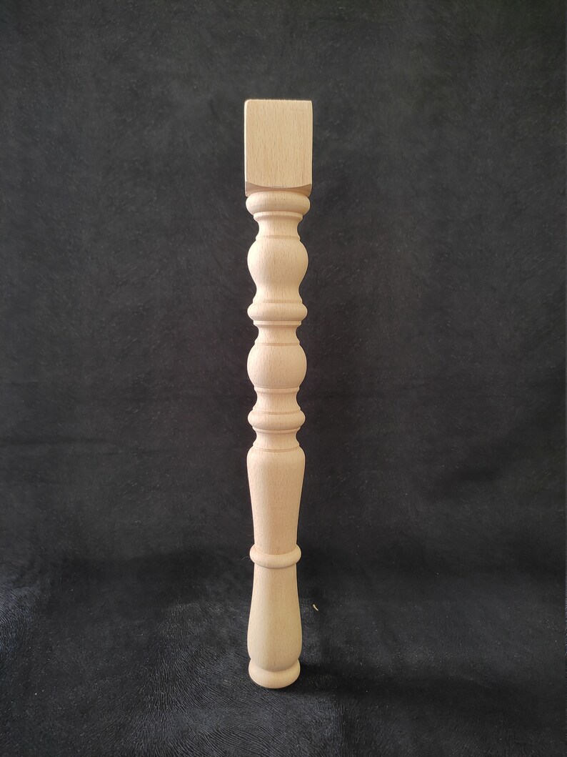 K&ouml;nnte beinhalten: Ein Tischbein aus Holz mit gedrehtem Design. Das Bein ist unbehandelt und hat eine quadratische Oberseite.