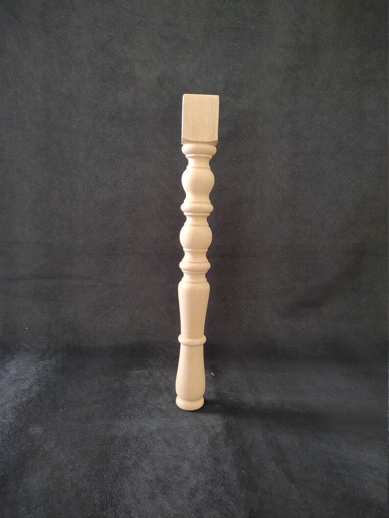 K&ouml;nnte beinhalten: Ein Tischbein aus Holz mit gedrehtem Design. Das Bein ist unbehandelt und hat eine quadratische Oberseite.