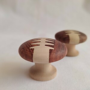 Op de afbeelding: Twee houten knoppen met een lichtbruin en donkerbruin houtnerfpatroon. De knoppen hebben een boomontwerp dat in de bovenkant is gegraveerd.