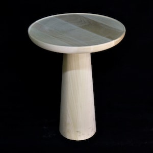 May include: A light wood side table with a round top and a tall, tapered base.