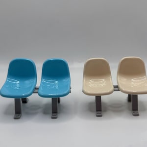 May include: Four small plastic chairs. Two are light blue, and two are beige. Each pair of chairs is connected by a gray bar and has gray legs. The chairs have a glossy finish and are arranged in a row.