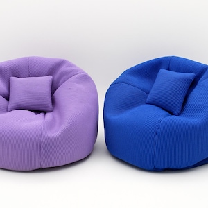Peut inclure: Deux petits poufs ronds avec une texture en tissu côtelé. Un pouf est violet clair et l'autre est bleu roi. Chaque pouf comporte un petit coussin rectangulaire assorti placé au centre de l'assise du siège.