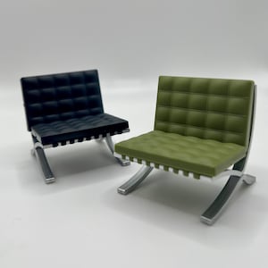 Op de afbeelding: Twee miniatuurstoelen met een chroom frame en gestoffeerde zittingen. Eén stoel heeft een zwarte zitting en de andere een groene zitting.