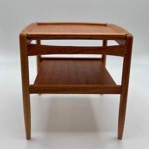 Pode incluir: Uma mesa auxiliar de madeira com duas prateleiras. A mesa tem um acabamento em madeira natural e é feita de madeira maciça.