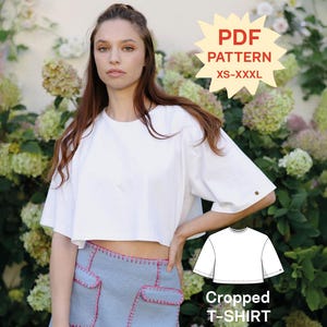 Pode incluir: Uma t-shirt branca curta com mangas curtas e decote redondo. A imagem inclui um gráfico de estrela amarela com o texto PDF PATTERN XS-XXXL e um desenho de linha da t-shirt rotulado como Cropped T-SHIRT.