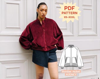 Puede incluir: Una chaqueta bomber de pana color rojo oscuro con cremallera frontal, mangas largas y dos bolsillos delanteros. La imagen incluye una etiqueta de patrón PDF para tallas XS-XXXL y un dibujo técnico Bomber Jacket AUDREY.