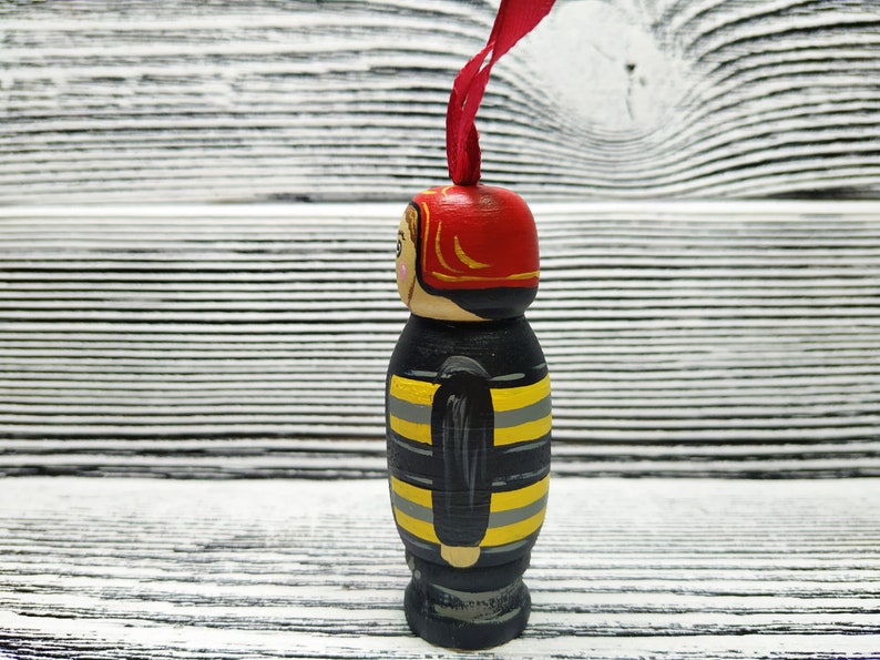 Pode incluir: Uma figura de madeira de um bombeiro vestindo um capacete vermelho e um uniforme listrado preto e amarelo. A figura &eacute; pintada com detalhes e tem uma fita vermelha presa ao topo do capacete.