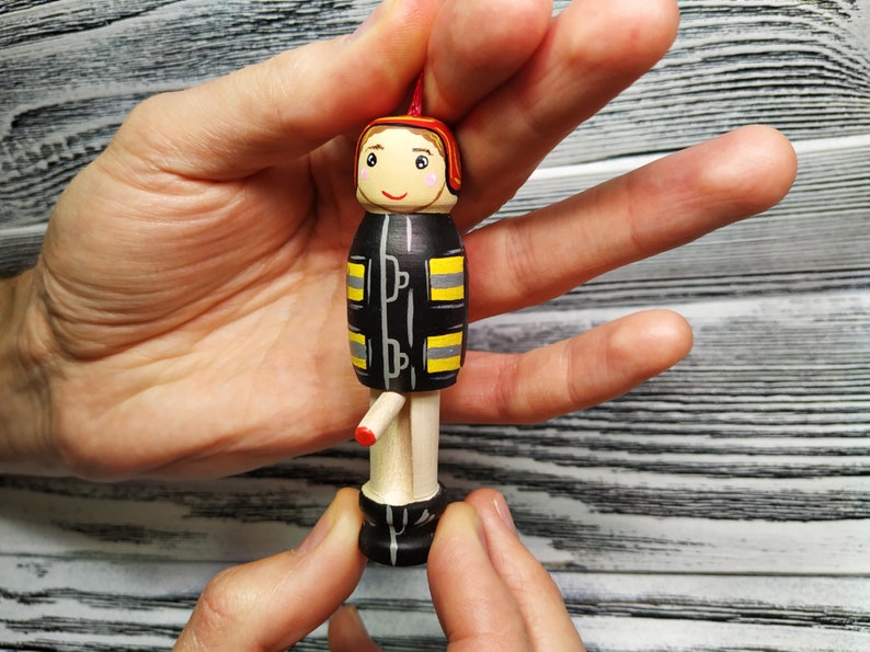 Pode incluir: Uma figura de madeira de um bombeiro vestindo um uniforme preto e amarelo com um capacete vermelho. A figura tem um rosto pintado com um sorriso e est&aacute; segurando uma mangueira vermelha.