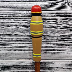 May include: A wooden figurine painted to look like a firefighter. The figurine is brown with yellow and gray stripes and a red hat.