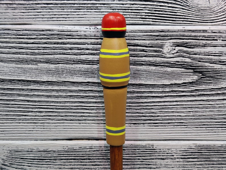 May include: A wooden figurine painted to look like a firefighter. The figurine is brown with yellow and gray stripes and a red hat.