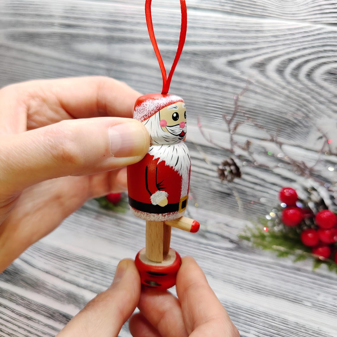 可能包含:一个迷人的圣诞老人圣诞挂饰,手绘于木质表面。他身穿带白色毛皮边的红色外套,留着白色的胡须,脸颊红润。该挂饰设计为可在底座上摇晃或晃动。它采用红白配色,非常适合悬挂在圣诞树上。