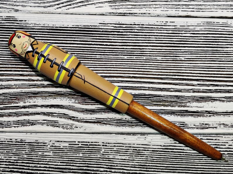 May include: A wooden pen with a brown and yellow painted design of a firefighter. The pen has a brown wooden barrel and a black ink tip.
