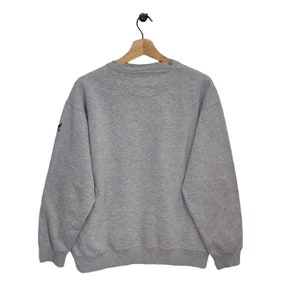 May include: A gray sweatshirt with a crew neck and long sleeves. The sweatshirt has a small logo on the left sleeve.
