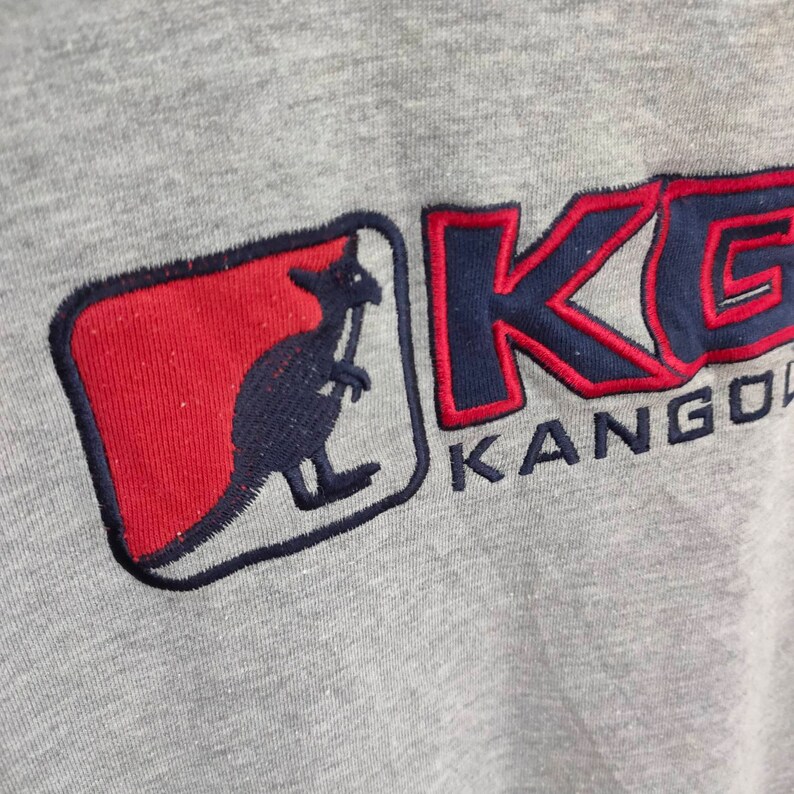 May include: A gray sweatshirt with a red and blue embroidered kangaroo logo and the text "KANGOL" in blue and red.