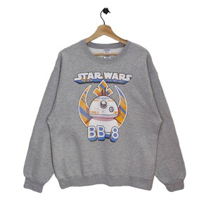Könnte beinhalten: Ein grauer Pullover mit einem Star Wars-Motiv mit BB-8. Das Motiv ist in einem blau-orange-weißen Farbschema gehalten.