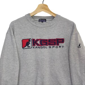 May include: Gray sweatshirt with a red and blue embroidered logo that says "KGSP KANGOL SPORT". A small kangaroo is in the logo. There is a small kangaroo logo on the right sleeve.
