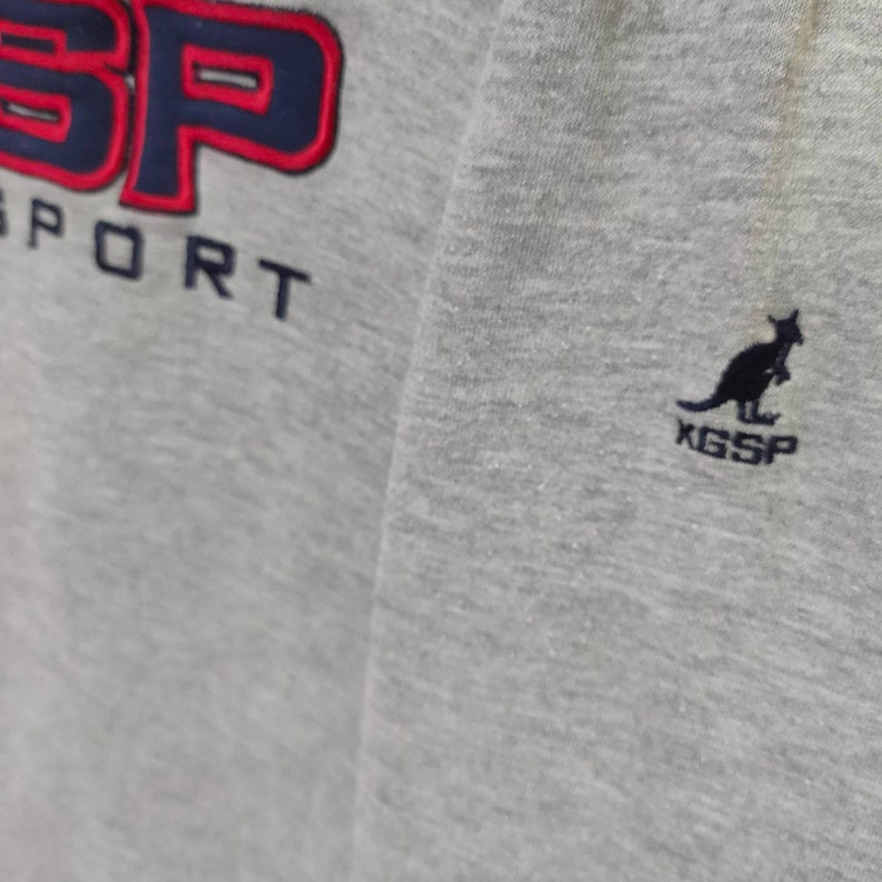 May include: Gray sweatshirt with a red and blue "SP" logo and the word "SPORT" underneath. A black kangaroo logo with "KGSP" underneath is on the right side of the sweatshirt.