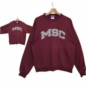 Könnte beinhalten: Burgunderfarbener Champion-Sweatshirt mit einem großen, grauen, gestickten Logo mit der Aufschrift "MSC Alumni".