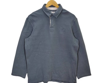 May include: A long-sleeved, dark blue rugby shirt with a white collar and a small embroidered logo on the chest.