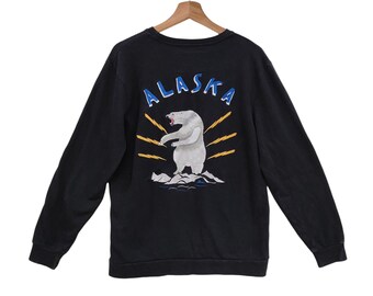 May include: Black sweatshirt with a graphic of a polar bear standing on ice, with the word "ALASKA" above it in blue letters. The bear is white with gray shading, and the background has yellow rays. The sweatshirt has long sleeves.