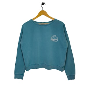 May include: A light blue sweatshirt with a white embroidered logo that says "Girls Surf Tour Billabong".