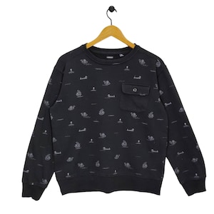 May include: Black sweatshirt with a small pocket on the left side. The sweatshirt has a repeating pattern of small white ships on a black background.