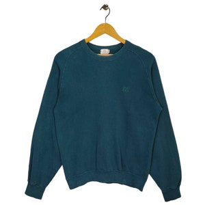 Könnte beinhalten: Ein blaugrüner Pullover mit einem kleinen gestickten Logo, das auf der Vorderseite "BVD" lautet.