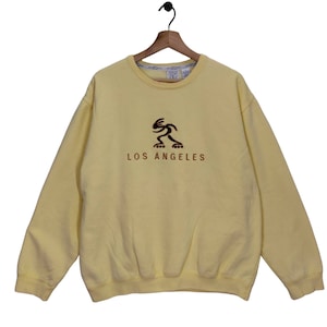 May include: A yellow sweatshirt with a brown and black graphic of a person roller skating and the text "LOS ANGELES" on the front.