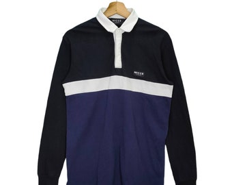May include: A long-sleeved rugby shirt with a black, white, and blue color block design. The shirt has a button-up collar and a small "NICCE" logo on the chest.