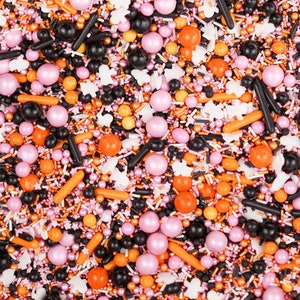 May include: A close-up of a mix of Halloween-themed sprinkles. The sprinkles include orange, black, and pink spheres, orange rods, black sticks, white ghost shapes, and small, colourful sprinkles. The overall effect is festive and colourful.