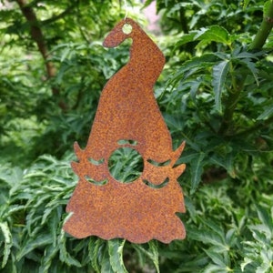 Può includere: Un ornamento in metallo arrugginito a forma di uccello stilizzato con un ritaglio circolare al centro. L'ornamento è appeso a una corda.