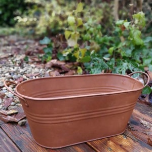 Könnte beinhalten: Ein rostiger brauner Metalltopf mit zwei Griffen. Der Topf ist oval geformt und hat ein rustikales Aussehen.