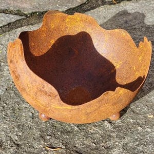 Könnte beinhalten: Ein rostiger Metalltopf mit einer einzigartigen, unregelmäßigen Form und drei kleinen Füßen. Der Topf ist aus recyceltem Metall gefertigt und hat ein rustikales, verwittertes Aussehen.