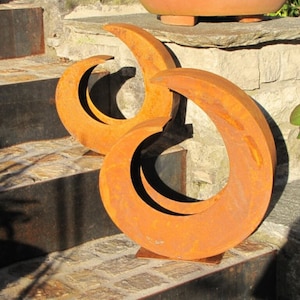 Peut inclure: Deux sculptures en métal rouillé en forme de croissant de lune, placées sur une marche en pierre. Les sculptures sont de couleur brun rougeâtre et ont une surface rugueuse et texturée.