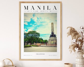May include: A framed print of a photograph of the Rizal Monument in Luneta Park, Manila, Philippines. The monument is a tall obelisk with a statue of Jose Rizal at the top. The park is a large, green space with trees and flowers. The print is in a wooden frame with a white mat.
