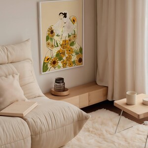 May include: A framed illustration of two women wearing white dresses with a floral pattern of yellow sunflowers. The background is a light peach color.