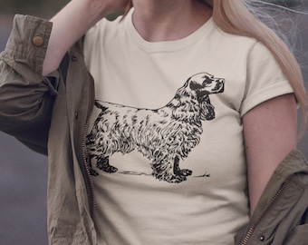 Könnte beinhalten: Cremefarbenes T-Shirt mit einer detaillierten Schwarz-Weiß-Illustration eines Cocker Spaniel-Hundes. Der Hund wird in einer stehenden Pose dargestellt, die seine charakteristischen Merkmale zeigt. Das T-Shirt wird von einer Person getragen.