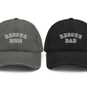 May include: Two distressed baseball caps, one gray with "RESCUE MOM" embroidered in white, and one black with "RESCUE DAD" embroidered in white.