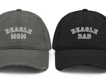 Könnte beinhalten: Zwei abgenutzte Baseballkappen, eine graue mit "BEAGLE MOM" in weiß gestickt und eine schwarze mit "BEAGLE DAD" in weiß gestickt.