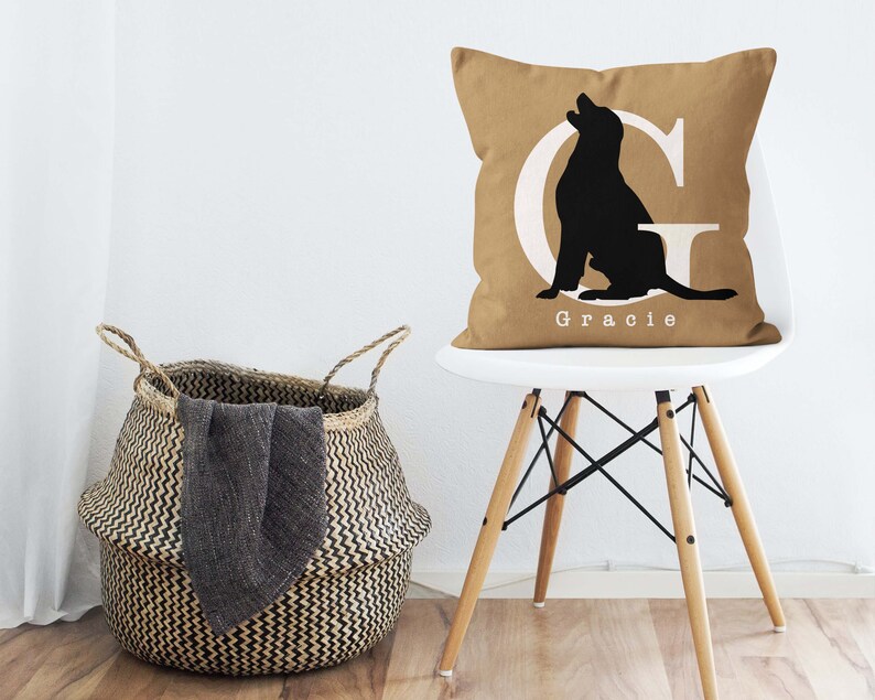 K&ouml;nnte beinhalten: Ein braunes Kissen mit einem wei&szlig;en Buchstaben G und einer schwarzen Silhouette eines Hundes, der im Buchstaben sitzt. Das Kissen tr&auml;gt den Namen "Gracie" unter dem Hund.