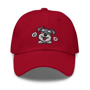 K&ouml;nnte beinhalten: Rote Baseballkappe mit einem gestickten Cartoon-Bild eines grau-wei&szlig;en Zwergschnauzers mit herausgestreckter rosa Zunge. Der Hund tr&auml;gt ein rotes Herz und hat eine Sprechblase mit der Aufschrift "Hallo".