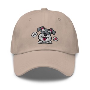 K&ouml;nnte beinhalten: Eine beige Baseballkappe mit einem gestickten Cartoon-Bild eines grau-schwarzen Zwergschnauzers mit herausgestreckter Zunge. Der Hund sagt "Hallo" in einer Sprechblase und hat ein rotes Herz in einer anderen Sprechblase.
