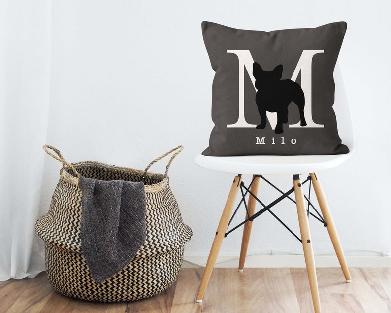 May include: A gray throw pillow with a white letter M and a black silhouette of a French bulldog. The pillow has the name "Milo" printed in white below the silhouette.