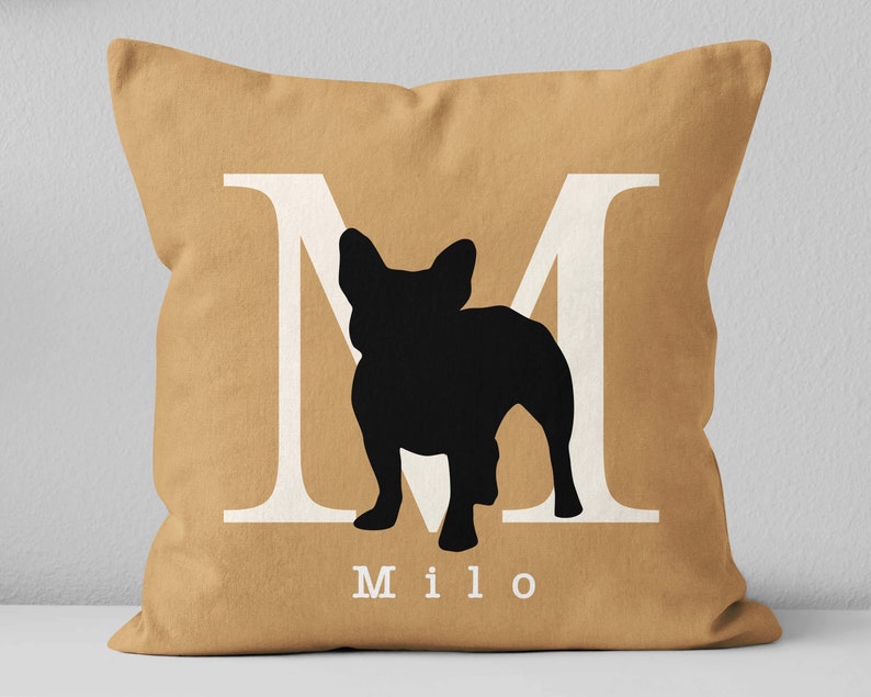 May include: A tan throw pillow with a white letter M and a black silhouette of a French Bulldog. The name Milo is printed below the silhouette.