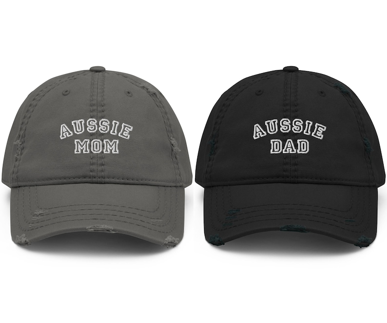 May include: Two distressed baseball caps, one gray with "Aussie Mom" embroidered in white, and one black with "Aussie Dad" embroidered in white.